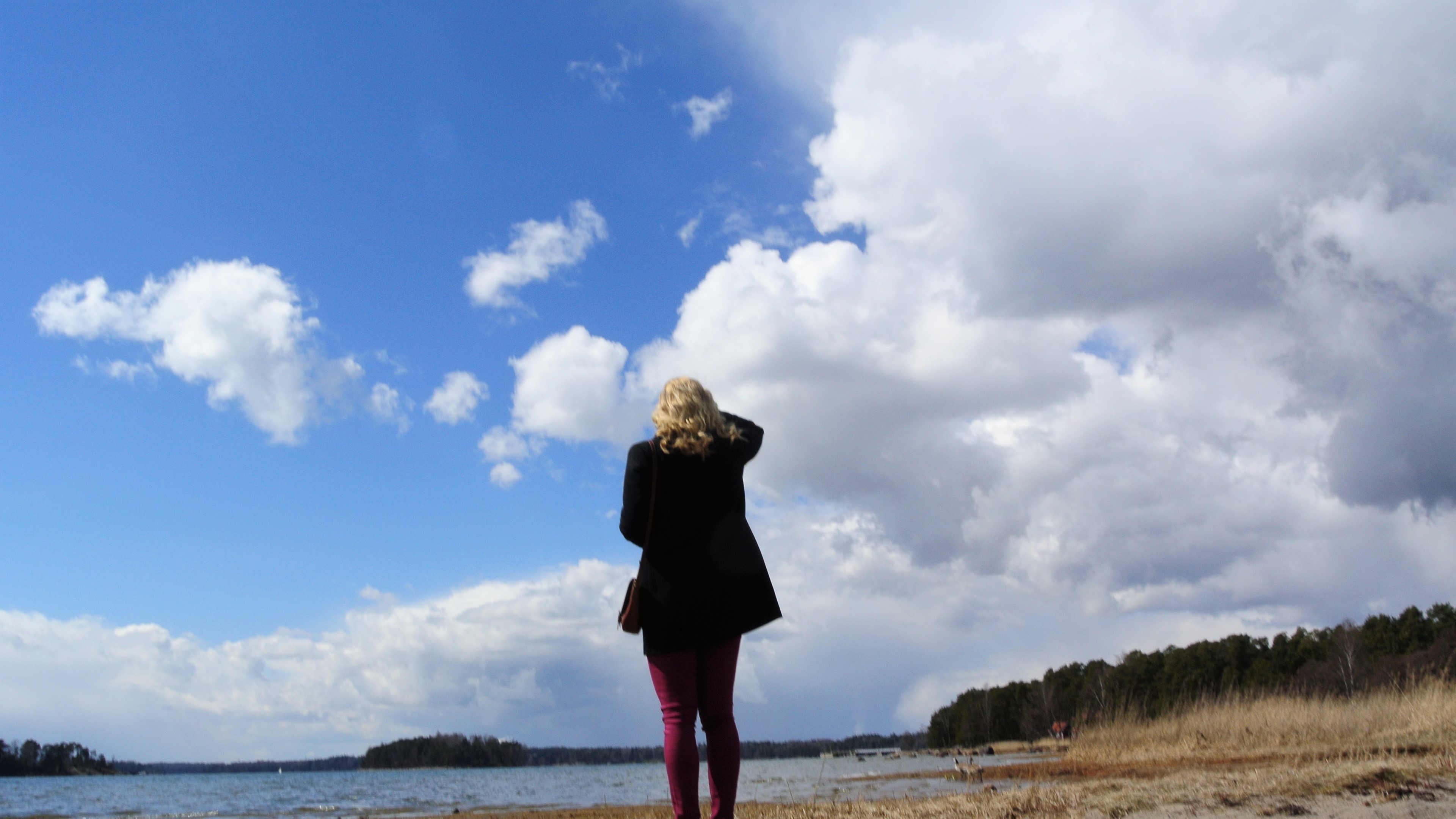 Kallahdenniemi A blonde girl standing on a beach looking at the blue sky and white clouds